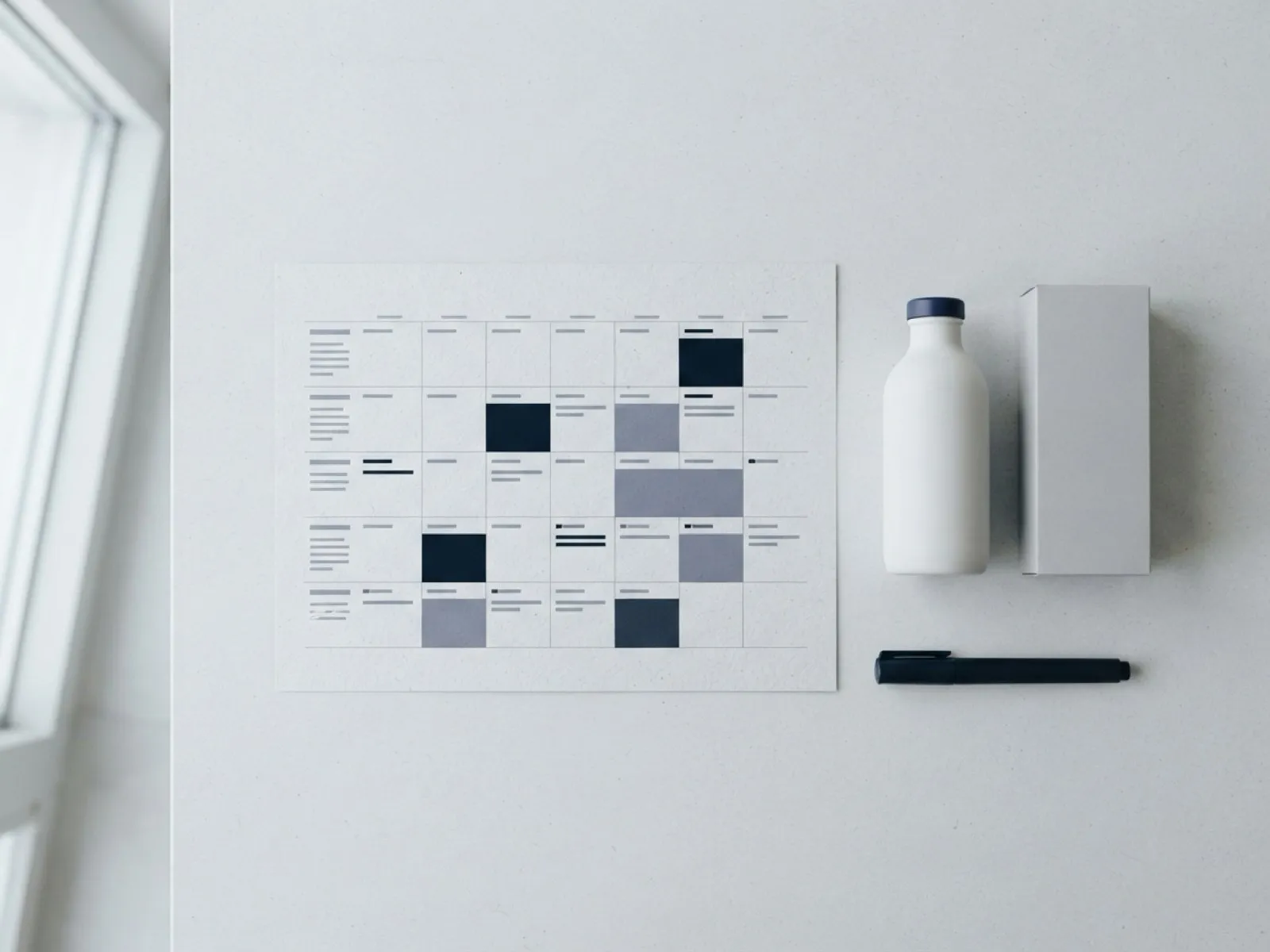 Calendario promocional impreso con semanas marcadas, junto a una botella y una caja sin marca.